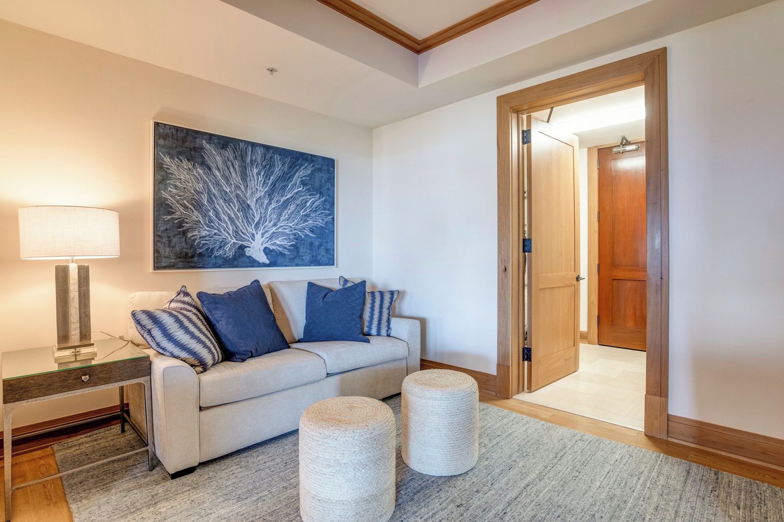 A living room with a sofa, a lamp, a painting, and a door leading to another room.
