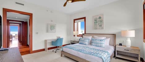 Quarto com cama, mesas de cabeceira, escrivaninha, cadeira, ventoinha no teto e vista para o exterior.