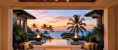 A luxurious indoor pool area with a sunset view, two sofas, and a fire feature.