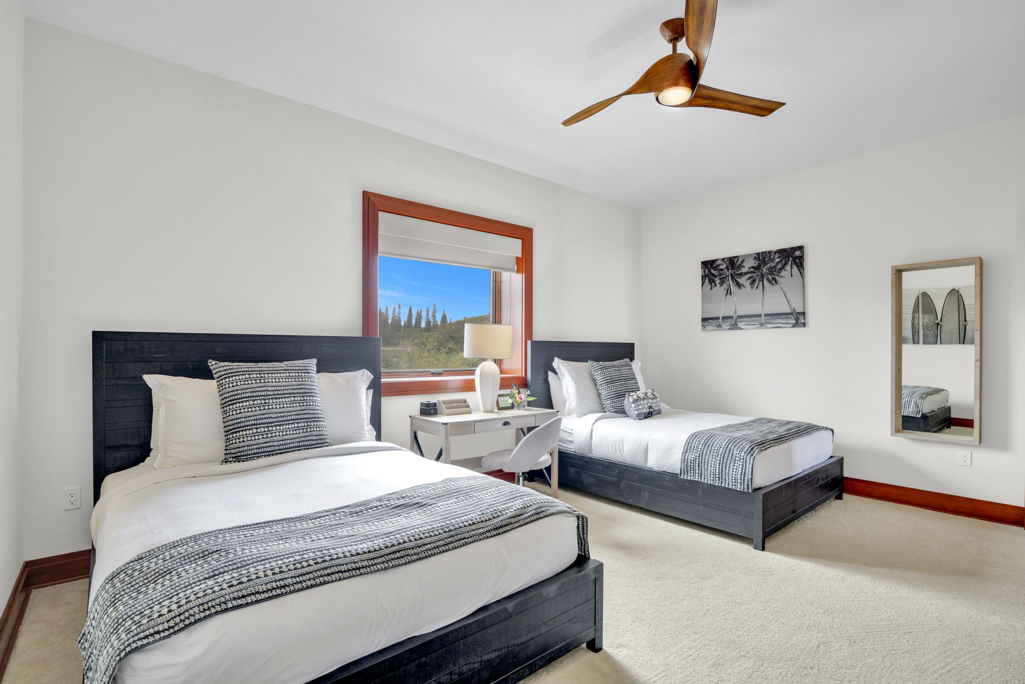 A hotel room with two beds, a desk, a chair, a ceiling fan, and artwork on the walls.