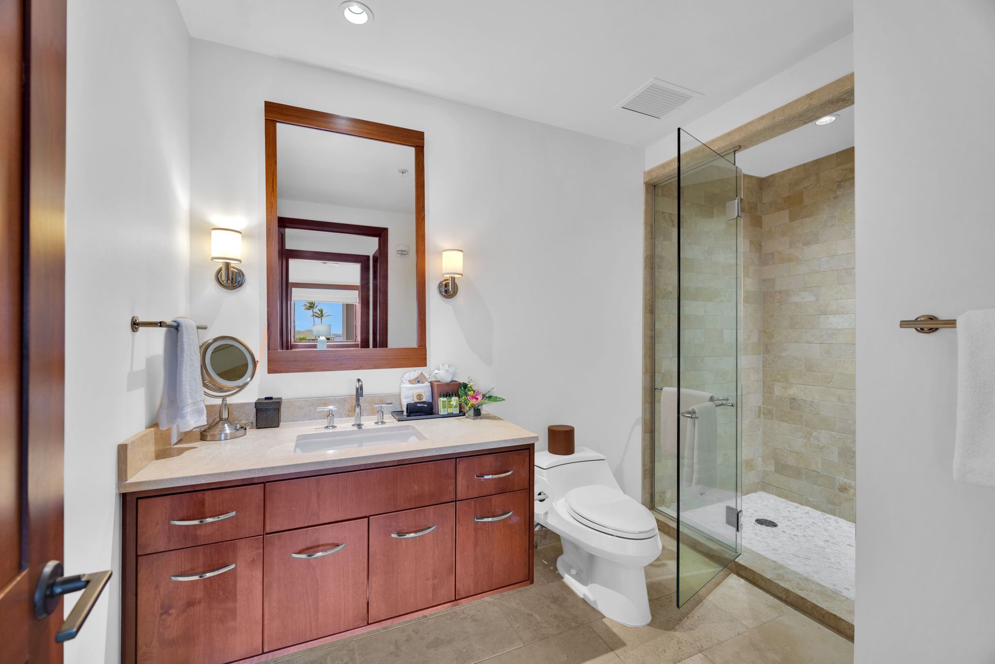 Un baño moderno con ducha envuelta en vidrio, tocador de madera y un espejo grande.