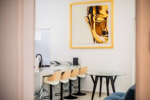 A modern kitchen with a marble countertop, bar stools, a round table, and a framed artwork on the wall.
