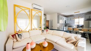 Een moderne woonkamer met een hoekbank, een eethoek met een glazen tafel, en een keuken op de achtergrond.