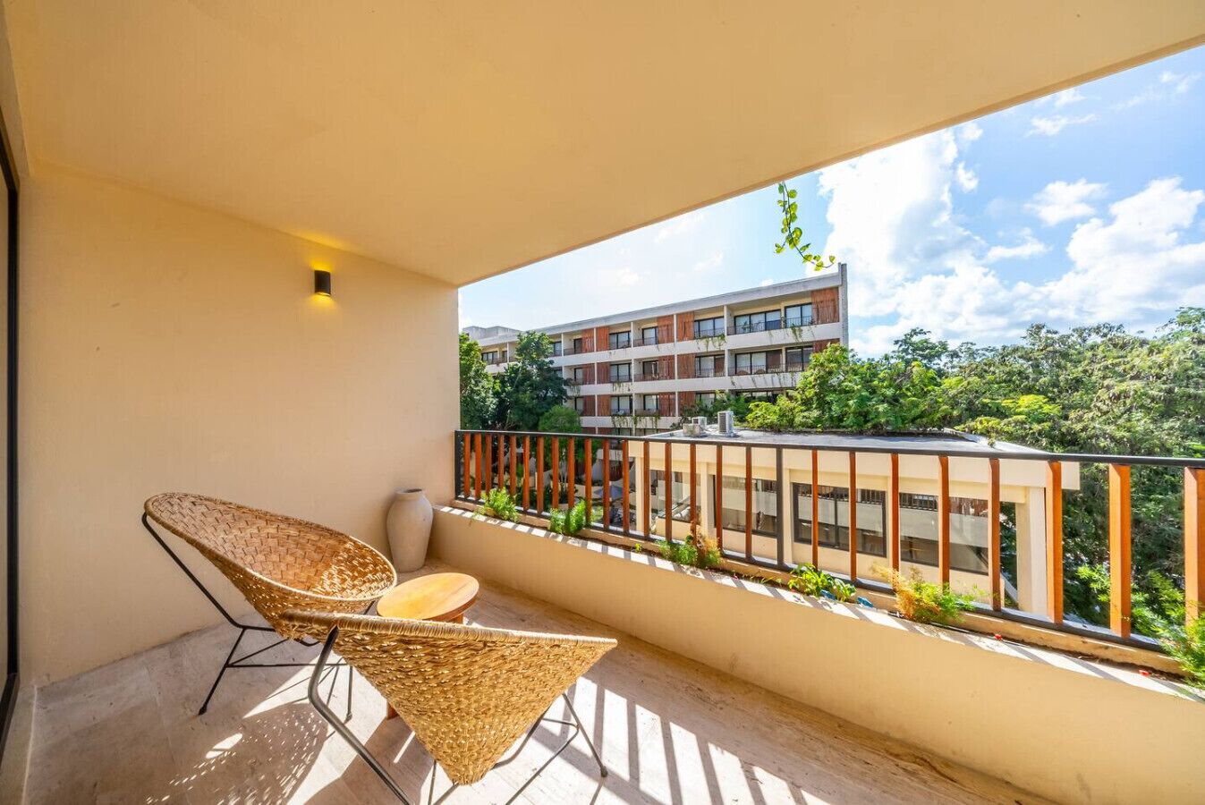 Un balcon doté de meubles en osier et offrant une vue sur un immeuble à plusieurs étages.