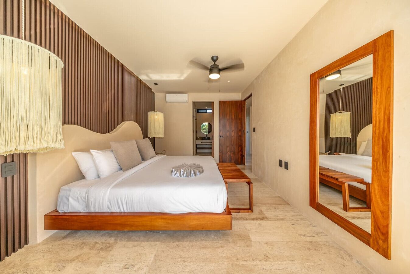 Een slaapkamer met een groot bed, een plafondventilator, een spiegel en een houten bankje.