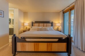 A bed with a wooden frame, two bedside tables with lamps, a large window with curtains, and a view of the outside. - The Plaza - Unit 642 (Mount Crested Butte)