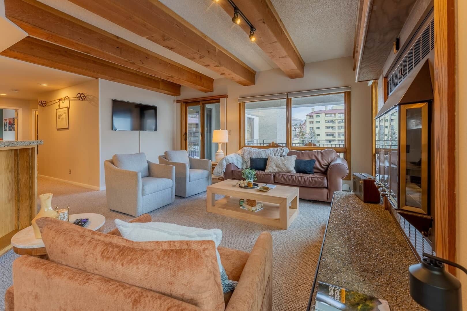 A spacious living area with a fireplace, a sofa set, a coffee table, and large windows offering a view of the city.