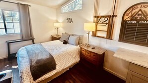 A bedroom with a bed, bedside tables, a window, a mirror, and a wall-mounted score board.