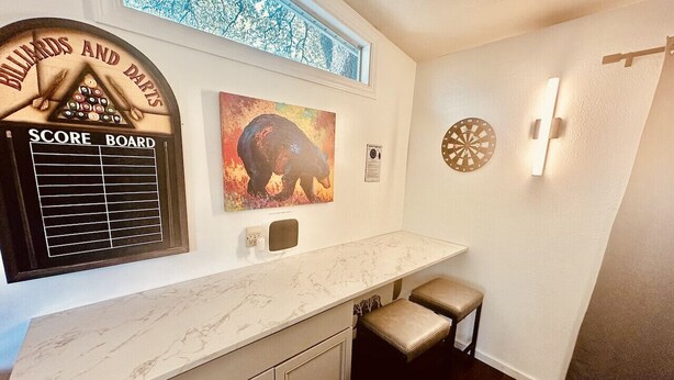 A bar area with a marble countertop, a dartboard, a score board, and a painting of a bear.