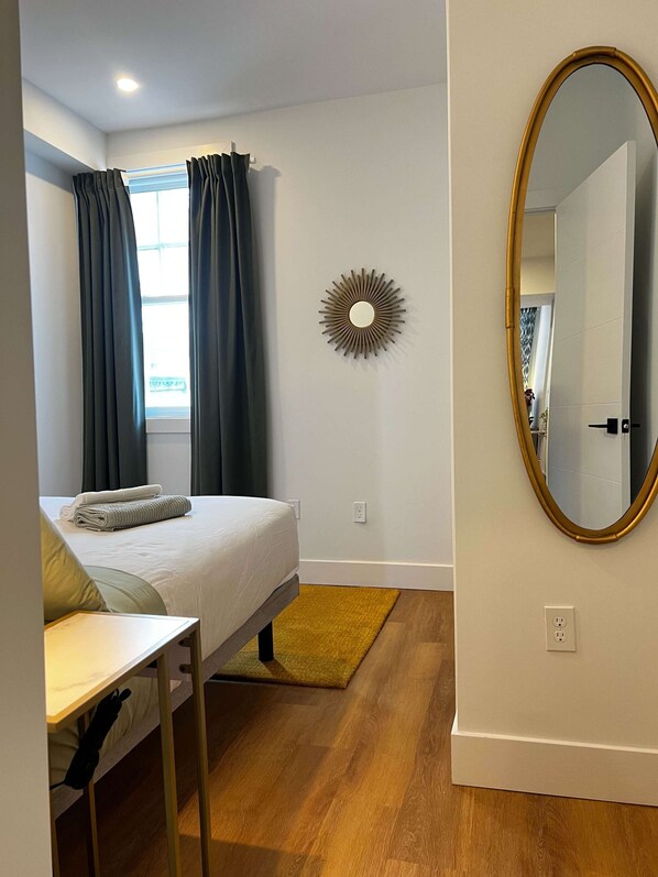A bedroom with a bed, a desk, a mirror, and a sunburst wall decoration.