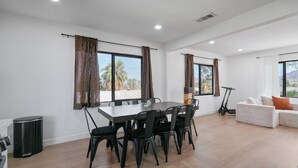 A modern living room with a dining area, large windows with curtains, a sofa, and an electric scooter. - Stargazing Dome with Hot Tub, E-Scooters, Game Room Retreat (Twentynine Palms)