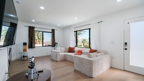 Una sala de estar moderna con un sofá modular, un telescopio y un ventanal con vistas a palmeras.
