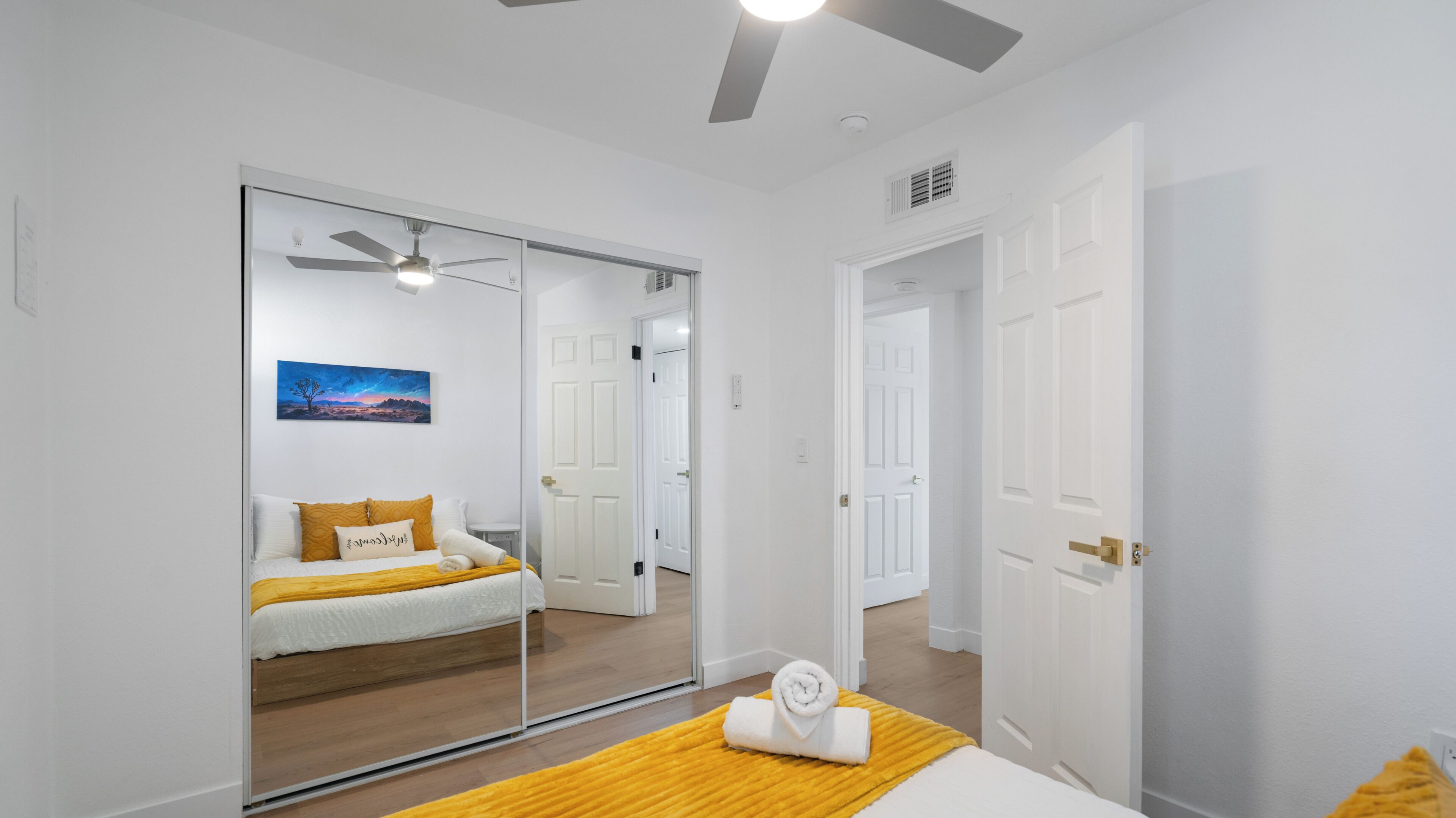 A bedroom with a bed, a mirror, a ceiling fan, and a nightstand.