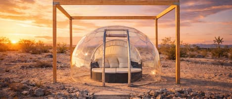 Una estructura tipo cúpula transparente con una escalera, una cama en su interior y un armazón de madera.
