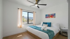 A bedroom with a bed, a ceiling fan, a window with curtains, a painting, and a bedside table. - Stargazing Dome with Hot Tub, E-Scooters, Game Room Retreat (Twentynine Palms)