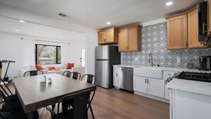 A modern kitchen with wooden cabinets, a stainless steel refrigerator, and a dining area with a table and chairs. - Stargazing Dome with Hot Tub, E-Scooters, Game Room Retreat (Twentynine Palms)