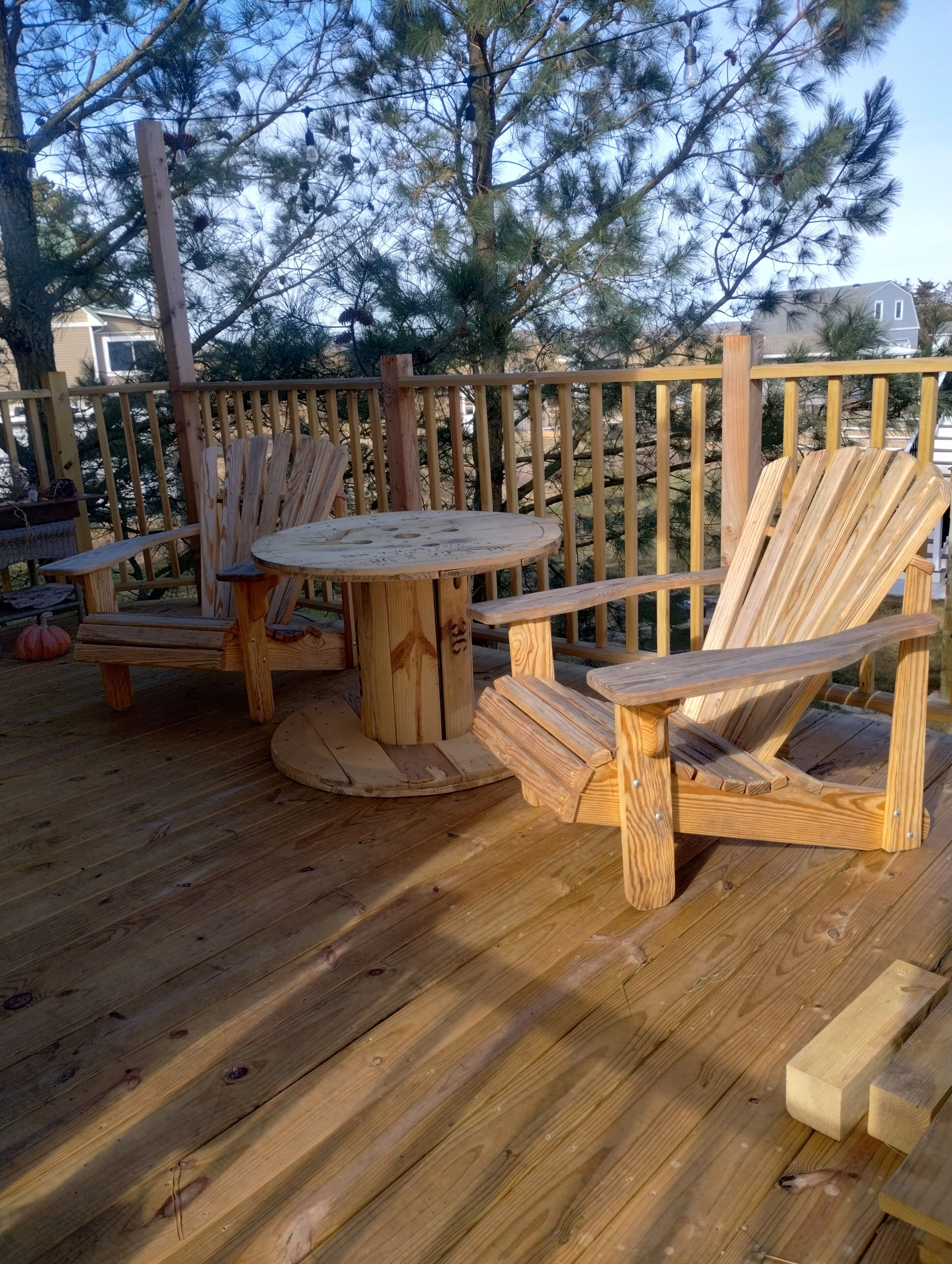 Een houten terras met een ronde tafel en twee Adirondack-stoelen.