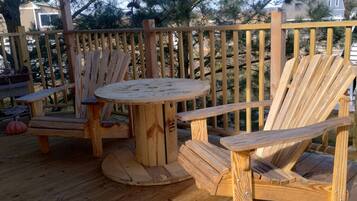 Een houten terras met een ronde tafel en twee Adirondack-stoelen.