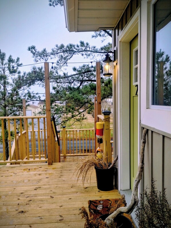 Una terraza de madera con barandilla, una planta en maceta y una ventana con vista a árboles.