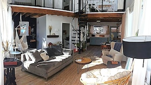 A spacious living area with a high ceiling, a staircase, and a view into the kitchen.