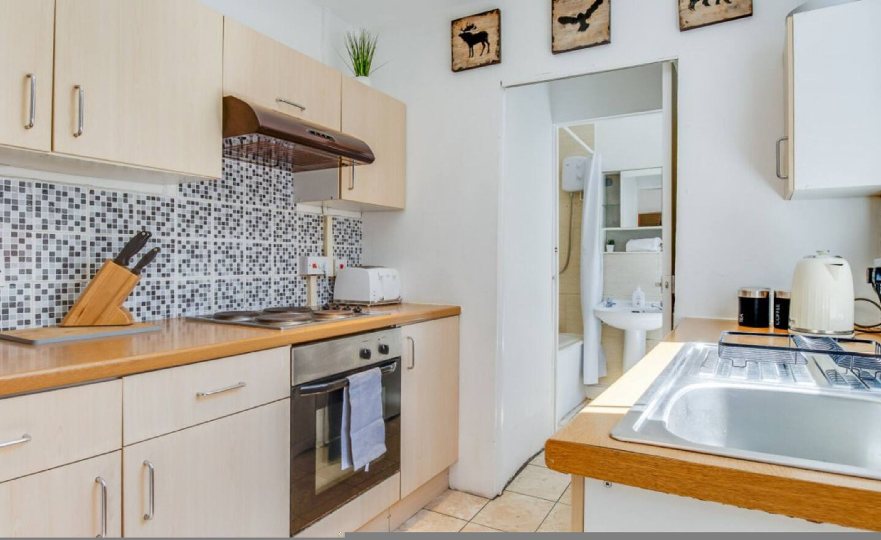 A compact kitchen with a tiled backsplash, a stove, a sink, and wooden cabinets.