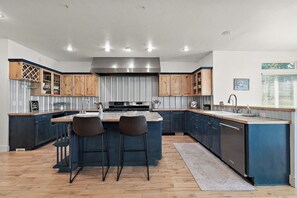 A modern kitchen with a central island, bar stools, wooden cabinets, stainless steel appliances, and a window with blinds. - Ultimate Group Getaway: 3 min from Lake, vineyards, event centers + Hot Tub (Caldwell)