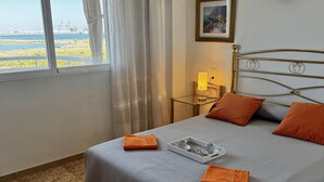 Habitación de hotel con cama, mesita de noche con lámpara, un cuadro en la pared y vistas al agua y edificios.