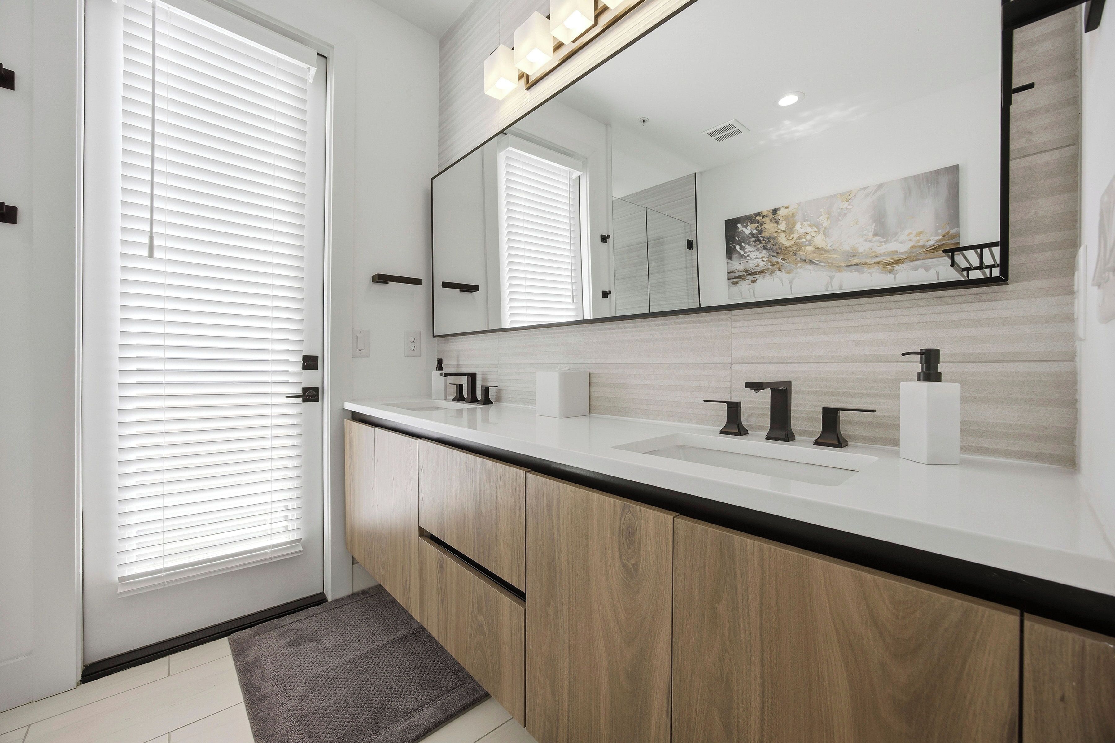 Een moderne badkamer met een grote spiegel, twee wastafels, houten kastjes en een grijze vloerkleed.