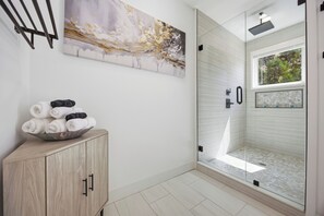Ein modernes Badezimmer mit Duschkabine aus Glas, einem Holzkabinet mit Handtüchern und einem großen abstrakten Gemälde an der Wand.