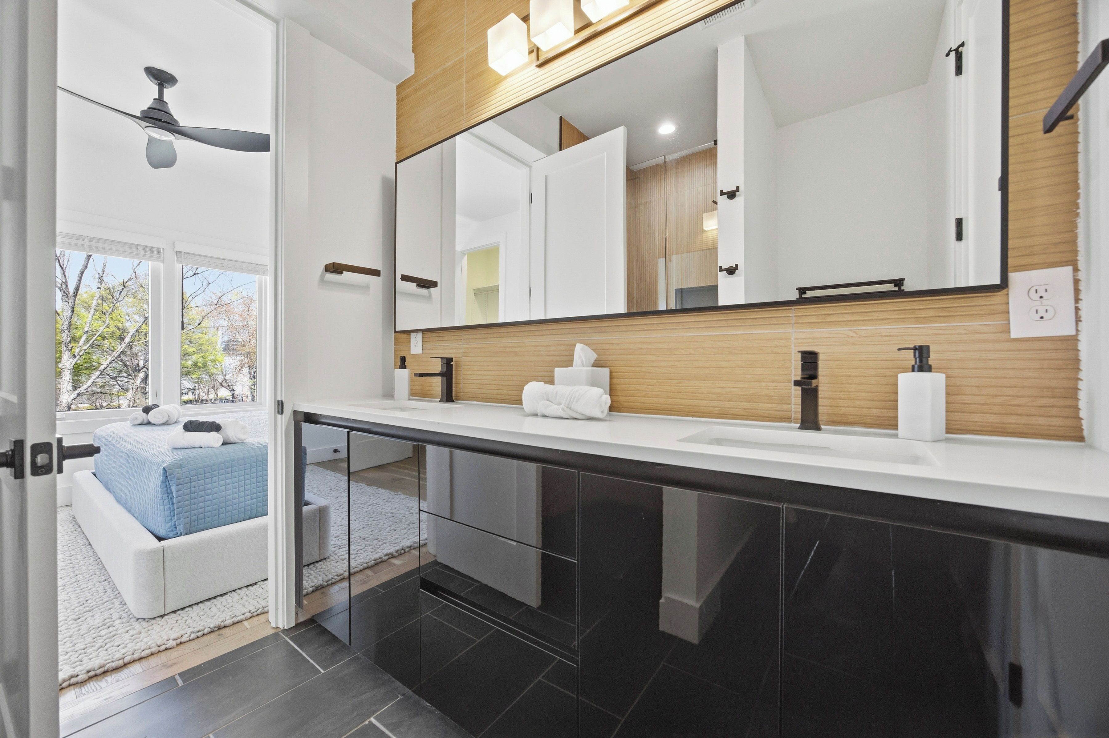 A modern bathroom with a large mirror, a ceiling fan, and a view of the outdoors.