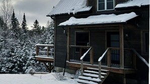 A wooden cabin with a porch and steps leading to the entrance, surrounded by snow-covered trees.