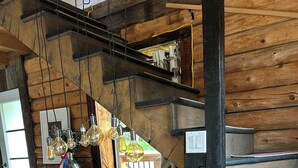 A rustic interior with a wooden staircase, a large flat-screen TV, and hanging light fixtures.