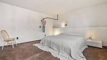 Une chambre à coucher comprenant un lit, une chaise, des tables de chevet et un luminaire fixé au mur.