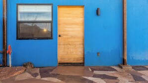 Ein blaues Gebäude mit einer Holztür, einem Fenster und einem eingepflasterten Eingangsbereich.