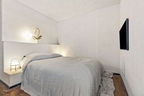 Une chambre à coucher avec un lit, une table de chevet avec une lampe et un téléviseur fixé au mur.