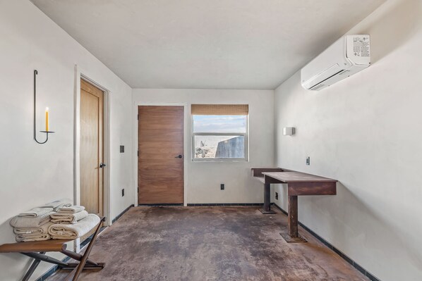 Un couloir avec une porte en bois, une fenêtre donnant sur un paysage agréable, un climatiseur fixé au mur et un banc avec des serviettes.