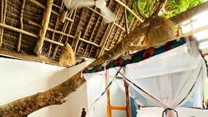 A room with a wooden bed, a thatched roof, and a hanging chair.