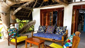 A wooden sofa with colorful cushions, a wooden coffee table, and a woven mat on a veranda.