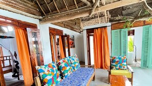 A room with a thatched roof, a bed with colorful pillows, a wooden chair, and a small table.