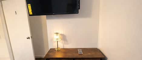 A room with a wooden desk, a black chair, a lamp, and a mounted TV.