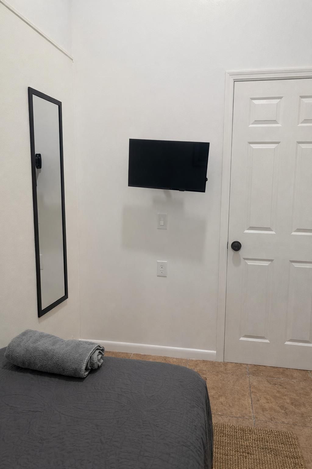 Una habitación con una cama, un televisor de pantalla plana en la pared, una puerta y un espejo.