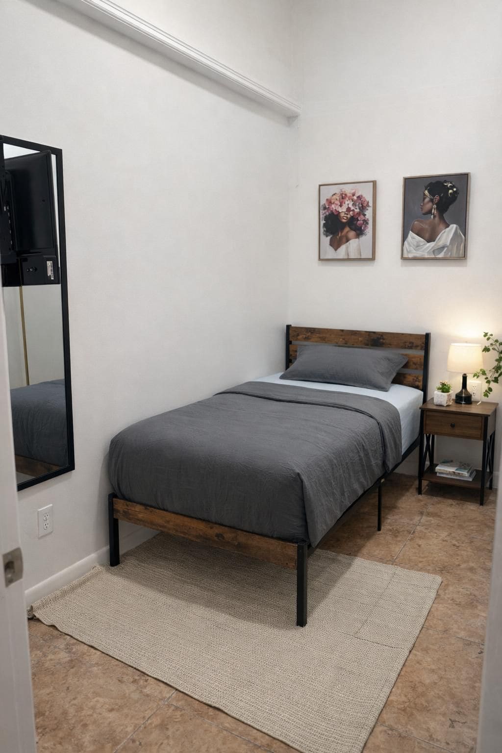 A bedroom with a bed, a nightstand, a lamp, a mirror, and two framed pictures on the wall.
