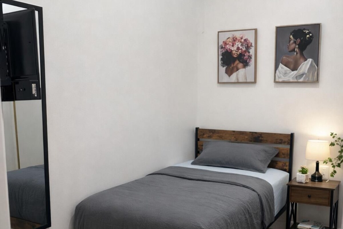 Une chambre à coucher comprenant un lit, une table de chevet, une lampe, un miroir et deux tableaux encadrés accrochés au mur.