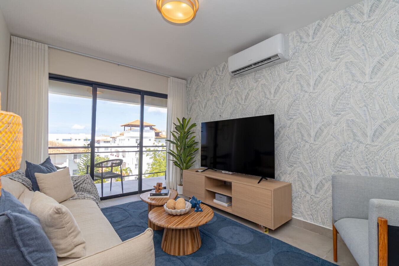 Een moderne woonkamer met een grote flatscreen televisie, een bank, een salontafel en een balkon met uitzicht op gebouwen.