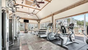 Ein Fitnessraum mit Trainingsgeräten, einem Deckenventilator und großen Fenstern.