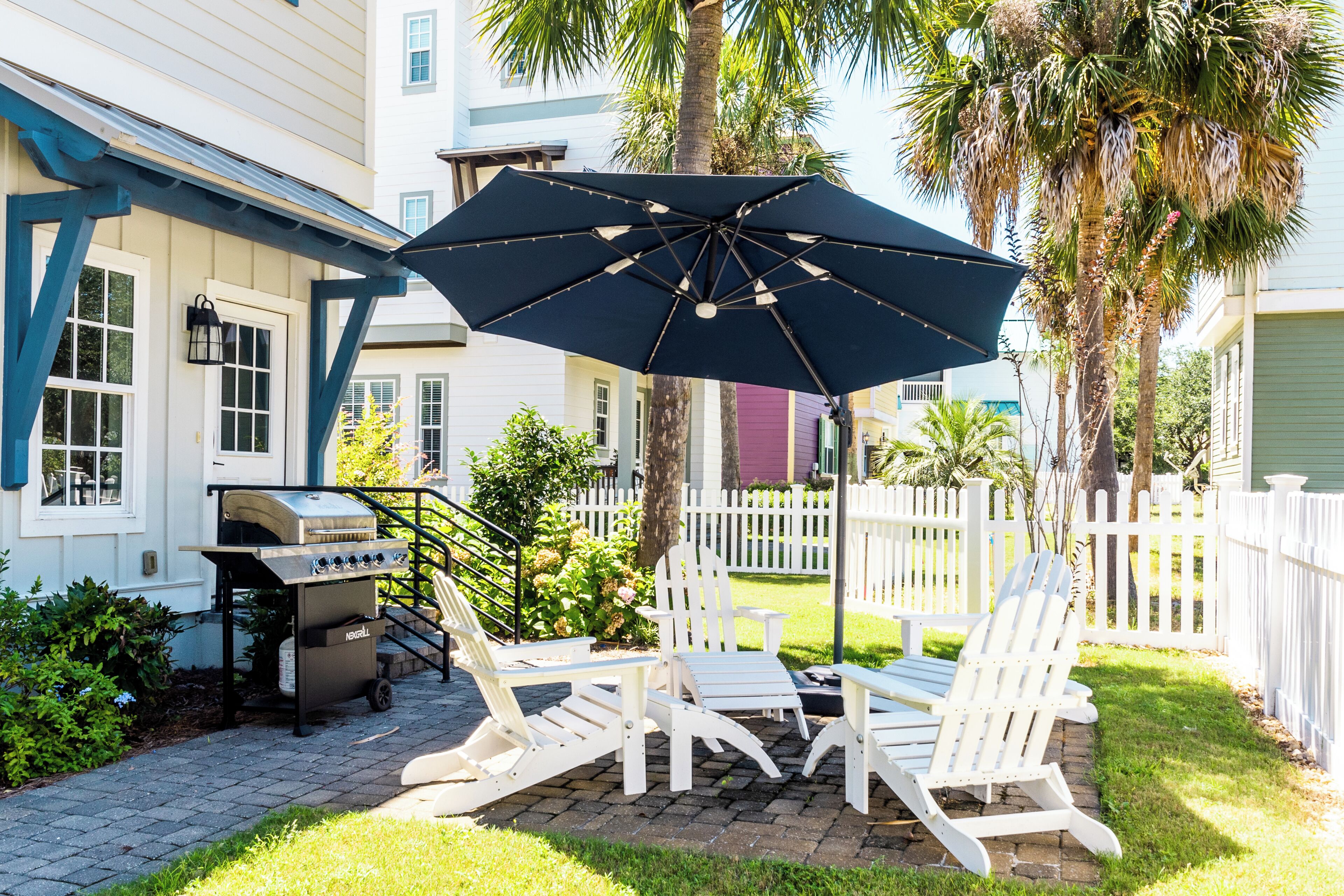 A patio with Adirondack chairs, a grill, and a large umbrella.