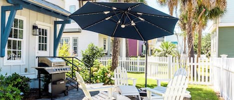 A patio with Adirondack chairs, a grill, and a large umbrella.