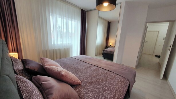 A modern hotel room with a large bed, a bedside table, a lamp, and a view of the hallway. - Sunny and Cozy Apartment (Brașov)