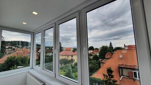 A room with large windows, a radiator, and a view of a residential area with houses and trees. - Sunny and Cozy Apartment (Brașov)