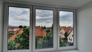 A window with three panes overlooking a residential area with red-tiled roofs and greenery. - Sunny and Cozy Apartment (Brașov)